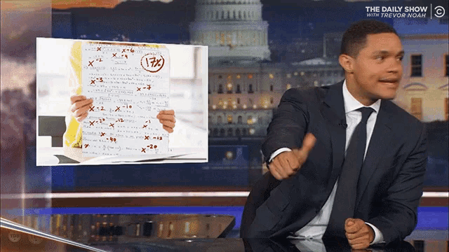 a man in a suit and tie is giving a thumbs up in front of a screen that says the daily show with trevor noah