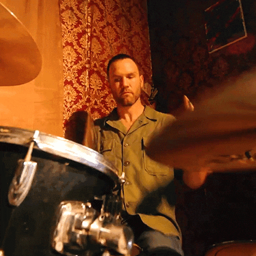 a man in a green shirt is playing drums in a dark room