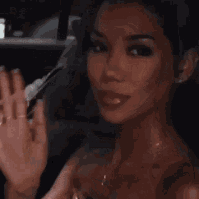 a woman in a gold dress is waving at the camera while sitting in a car .