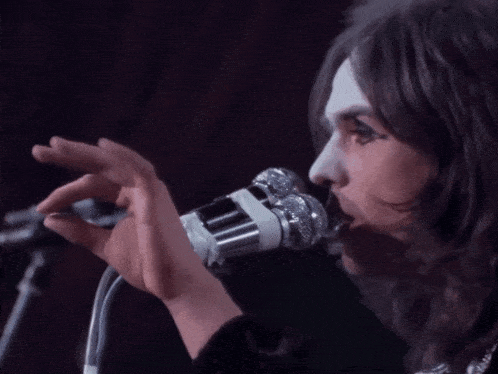 a close up of a person singing into a microphone with a purple background