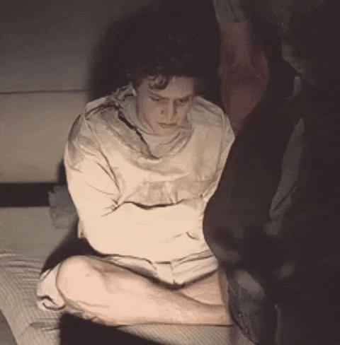 a man in a straight jacket is sitting on the floor with his arms crossed .