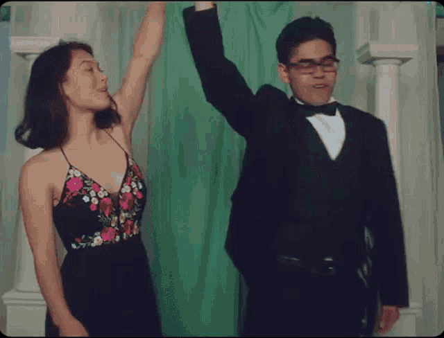 a man in a tuxedo and a woman in a dress are dancing in front of a green curtain .