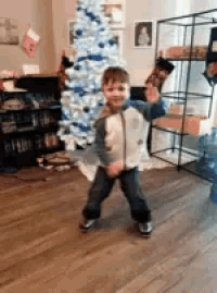 a young boy is dancing in front of a white christmas tree .