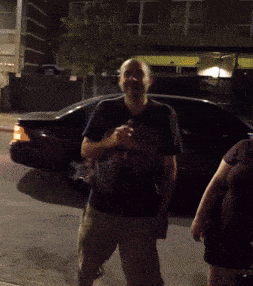 a man standing in front of a car holding a bottle of beer