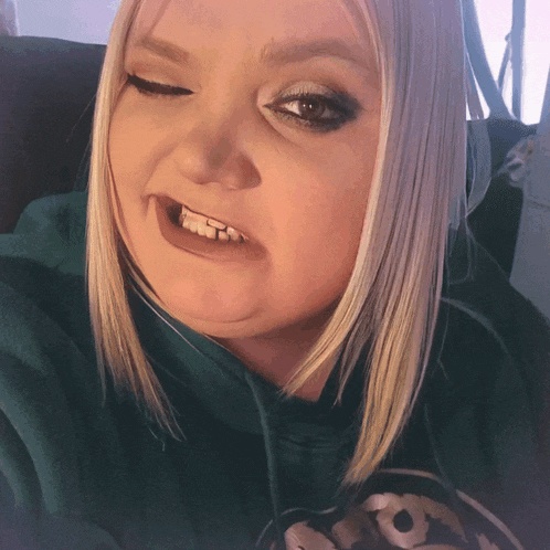 a woman with blonde hair wearing a green sweatshirt with a skull on it