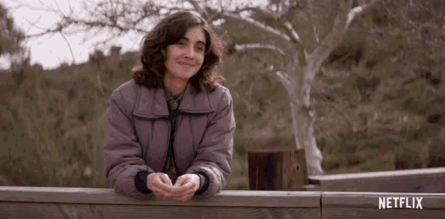 a woman in a purple jacket is giving a thumbs up in front of a sign that says netflix
