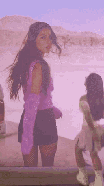 a woman in a purple top and black shorts is standing next to a car