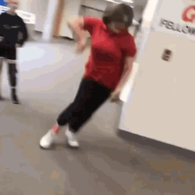 a woman in a red shirt and black pants is dancing on the floor .