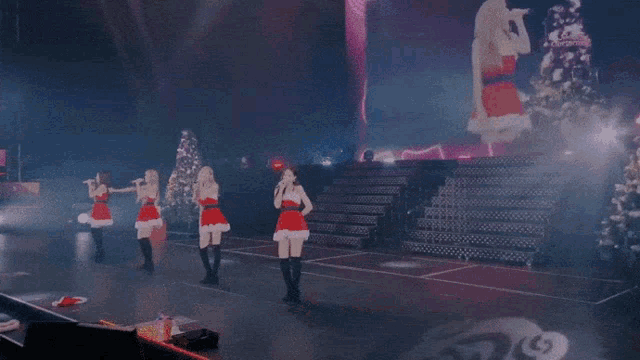 a group of women dressed in santa outfits sing on a stage