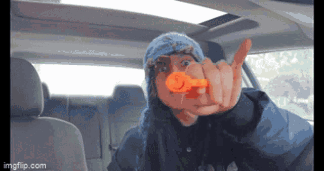 a person in a car is pointing at the camera with an orange object in their hand