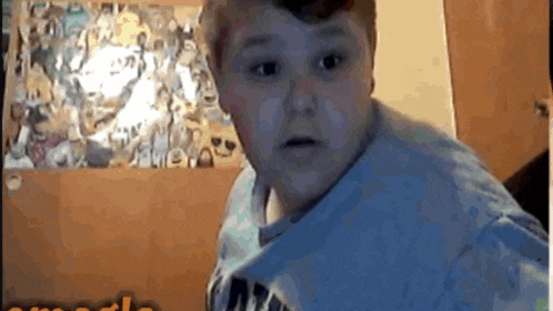 a boy in a blue shirt is standing in front of a wall with pictures on it