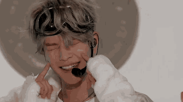 a young man wearing goggles and a microphone is smiling and covering his ears .