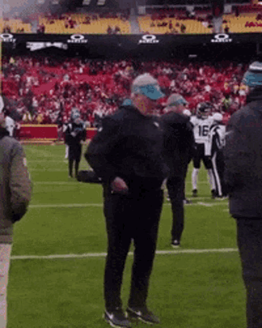 a man in a blue hat is standing on a football field in front of a crowd