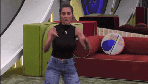 a woman in a black top and jeans is dancing in front of a couch