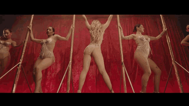 a group of women are dancing on a stage with a red curtain behind them