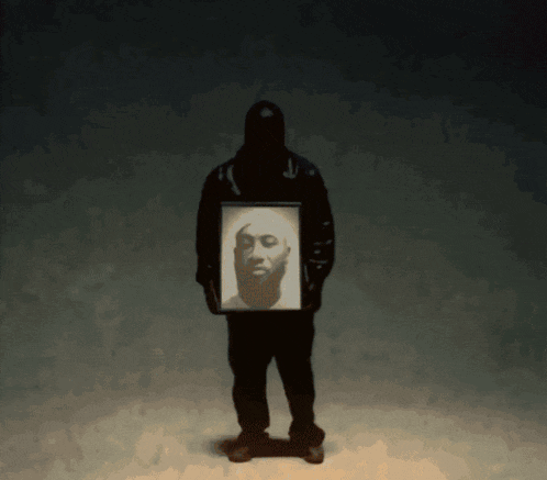 a man in a hooded jacket holds a picture of a man 's face