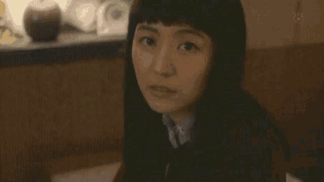 a woman with long black hair is sitting at a table and smiling at the camera .