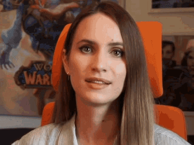 a woman sits in an orange chair in front of a world of warcraft poster