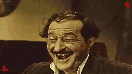 a man with a mustache and glasses is laughing with his eyes closed .
