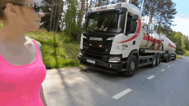 a woman in a pink tank top is standing in front of a scania truck