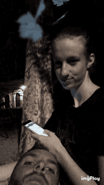 a man and a girl are looking at a cell phone and the girl is wearing a black shirt that says body