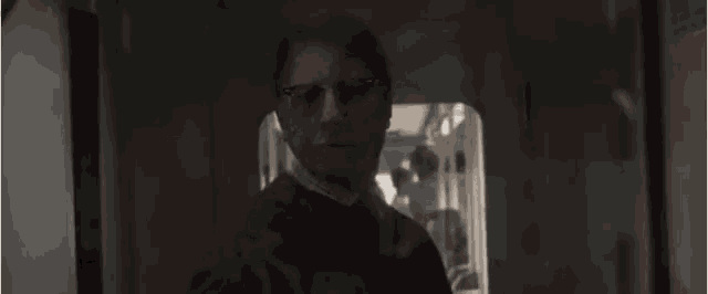 a man wearing glasses is standing in a dark room looking up at the sky .