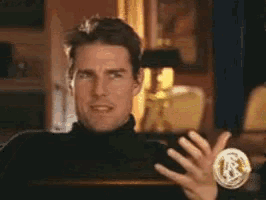 a man in a black turtleneck is laughing in a room with a coin in the foreground .