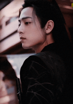 a man with long black hair and a black jacket looks to the side