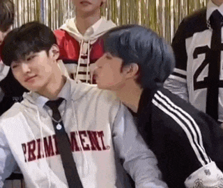 two young men are kissing each other in front of a crowd of people .
