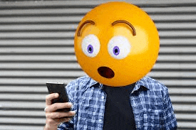 a man is holding a cell phone with a smiley face on his head .