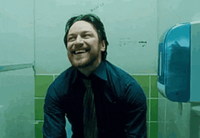 a man in a blue shirt and tie is sitting in a public restroom and smiling .