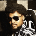 a man with a beard wearing sunglasses and a plaid shirt is sitting in a chair .