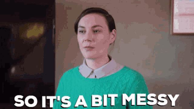 a woman in a green sweater is standing in front of a sign that says so it 's a bit messy .