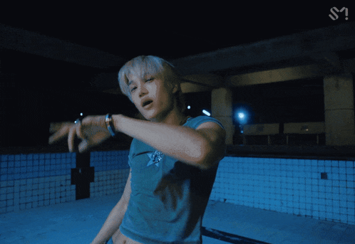 a man in a crop top and ripped jeans stands in an empty pool at night