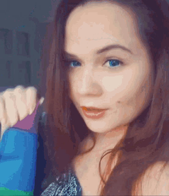 a woman with blue eyes is holding a rainbow flag in her hand