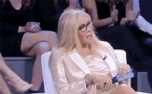 a woman in a white jacket and glasses is sitting in a chair