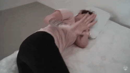 a woman is laying on a bed with her hands on her face and covering her face .
