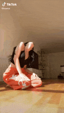 a woman in a black top and orange pants is kneeling down on the floor ..
