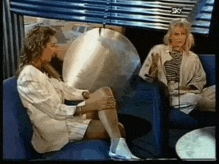 two women are sitting on a couch talking to each other in front of a microphone .