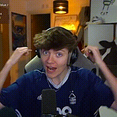a young man wearing headphones and a blue shirt is sitting in front of a microphone and making a funny face .