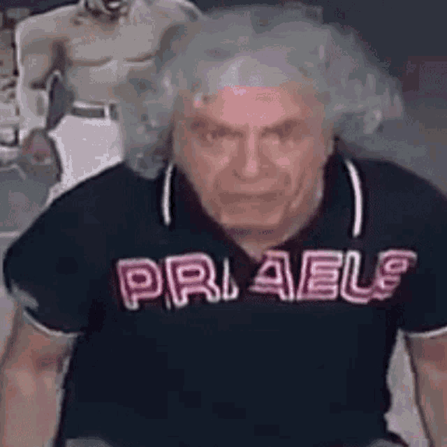 a man with curly hair is wearing a black polo shirt with the word pri ael written on it .