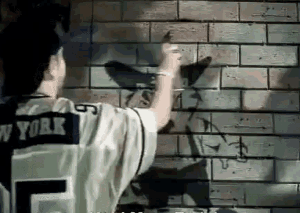 a man in a new york jersey is spray painting a picture of a bird on a brick wall .