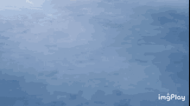 a blue airplane is flying in the sky with imgplay written on the bottom right