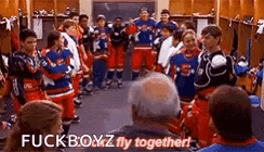 a group of hockey players are standing in a locker room with a man sitting in front of them .