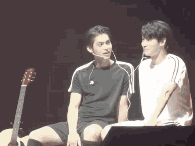 two men are sitting next to each other on a stage with a guitar .