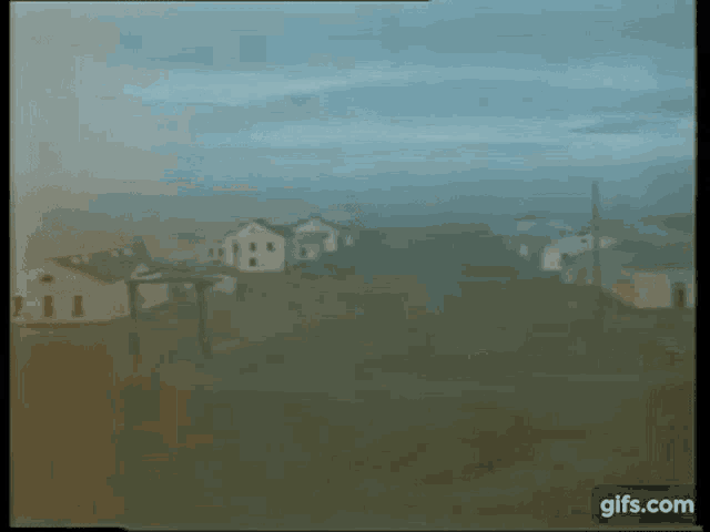 a blurry picture of a field with houses and trees in the background
