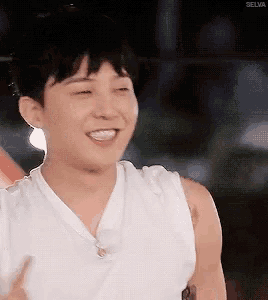 a young man in a white tank top is smiling and waving his hand .
