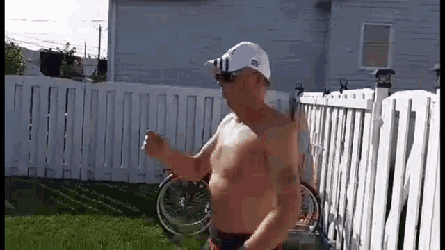 a shirtless man is standing in front of a white fence holding a bottle of water .