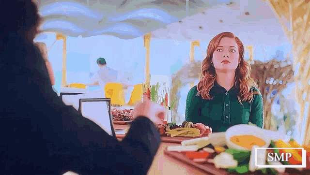 a woman in a green shirt sits at a table with a smp logo