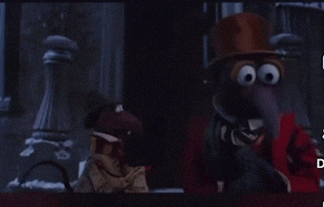a man in a top hat is talking to another man in a red coat and scarf with the words " what " above him
